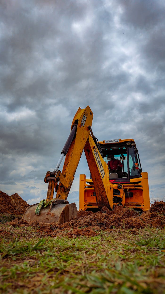 Yellow bulldozer working on a grassy field under cloudy skies.